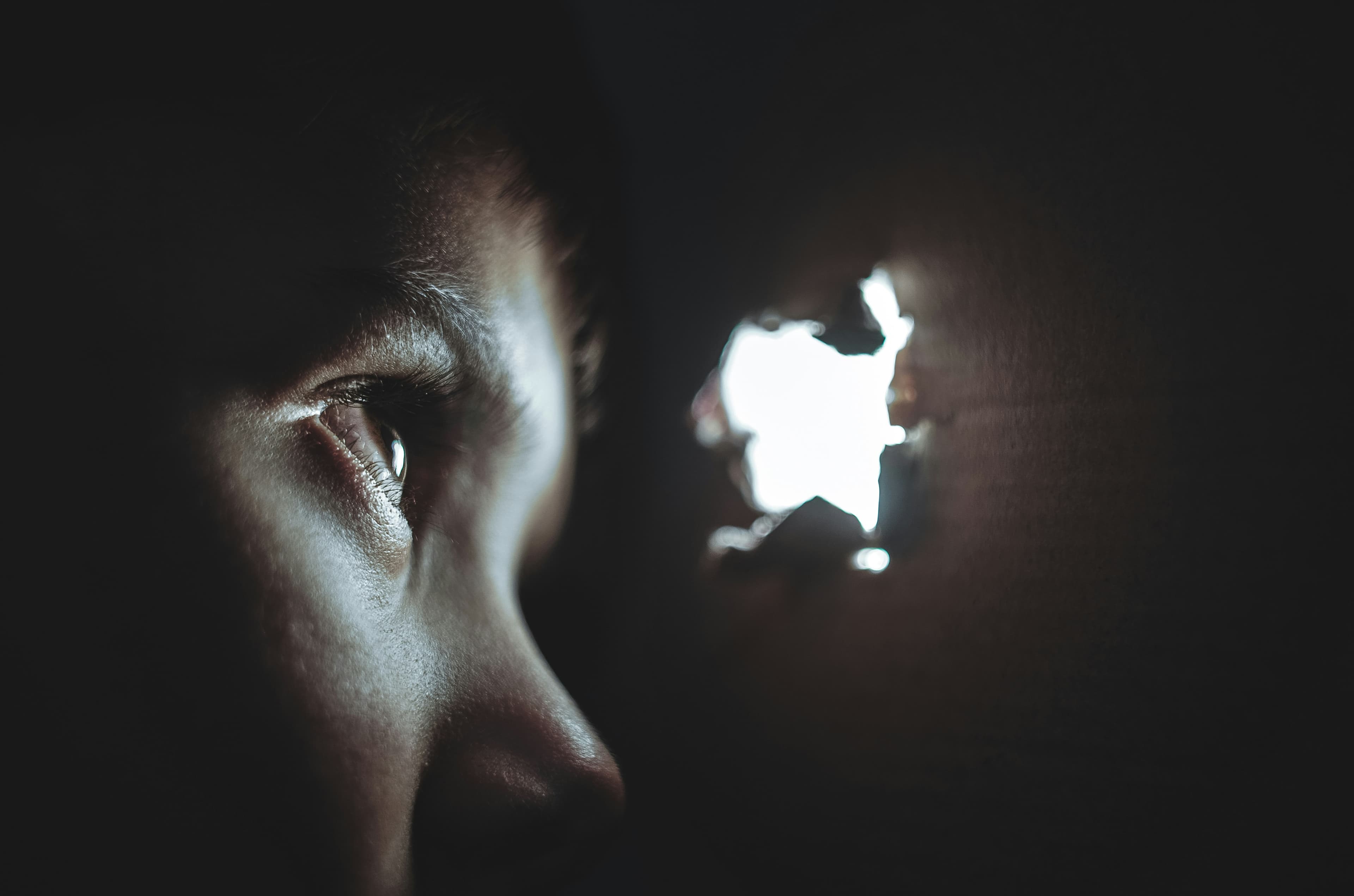 An eye peering through a hole in a dark wall